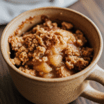 Apple crisp in a mug steaming hot with golden oat topping in terracotta ceramic mug