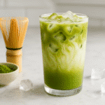 Iced matcha latte recipe in tall glass with layered green matcha and creamy milk on marble counter